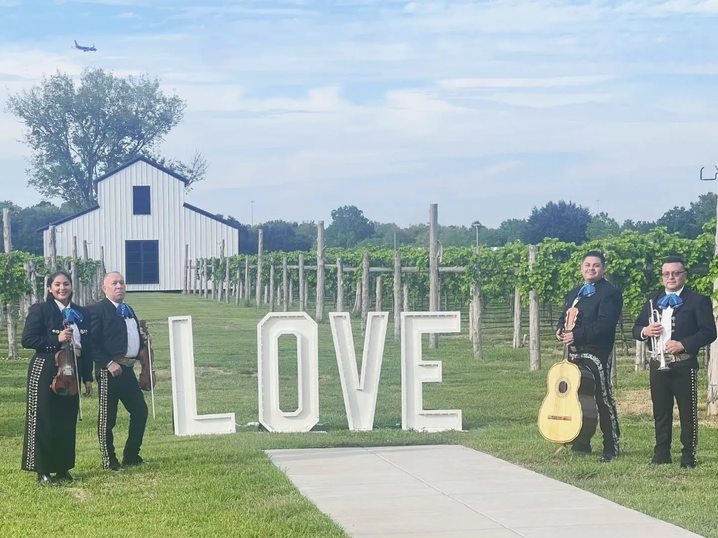 Mariachi band near large "LOVE" sign outdoors.