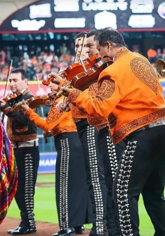 Mariachi band performing in vibrant orange outfits.